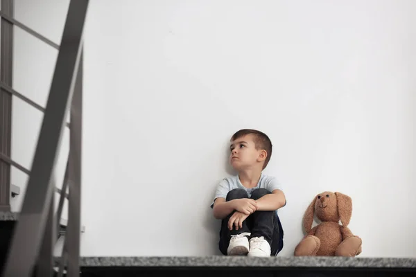 Triste menino com brinquedo sentado perto da parede branca — Fotografia de Stock