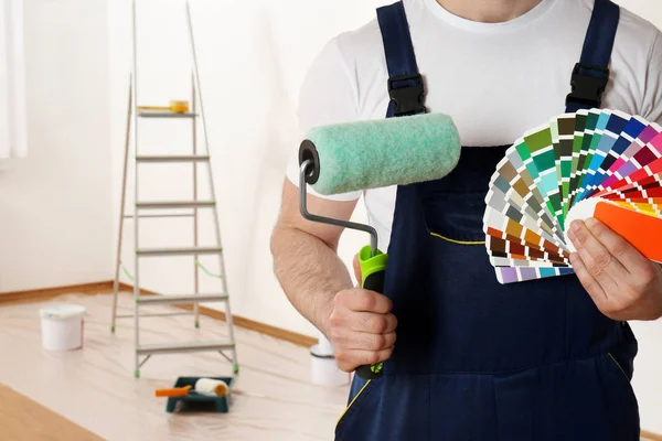 Decorador masculino com rolo de pintura e amostras de paleta de cores em sala vazia, close up. Espaço para texto — Fotografia de Stock