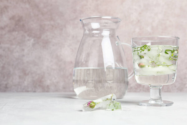Glass with floral ice cubes and water near jug on table. Space for text