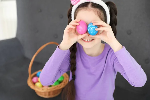 Маленькая девочка держит пасхальные яйца возле глаз дома — стоковое фото