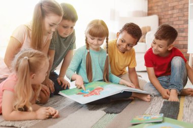 Yerde oturan sevimli küçük çocuklar ve birlikte kapalı kitap okuma