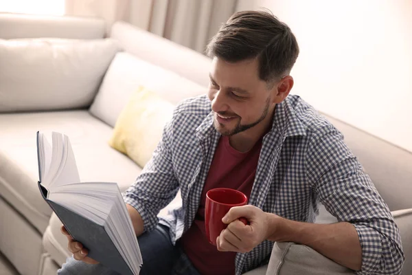 Schöner Mann liest Buch zu Hause auf dem Sofa — Stockfoto