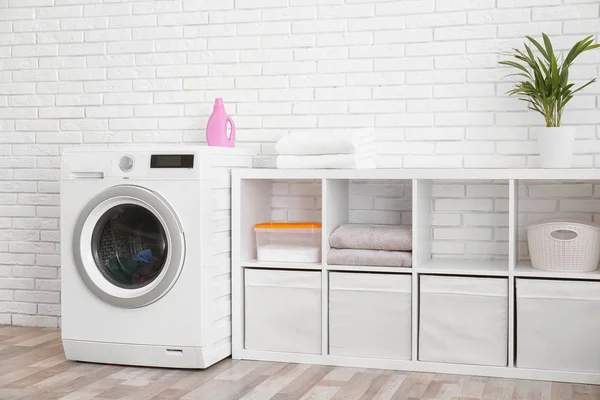 Máquina de lavar roupa moderna perto da parede de tijolo no interior da lavanderia — Fotografia de Stock