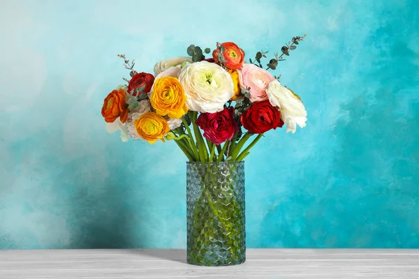 Ваза з красивими квітами рунункули на столі на кольоровому фоні — стокове фото