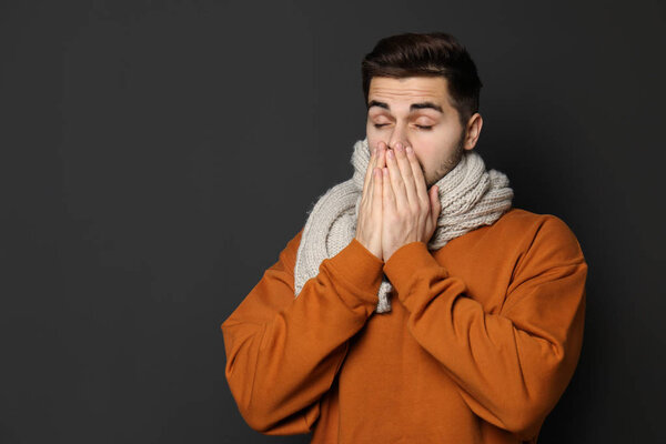 Handsome young man coughing against dark background. Space for text