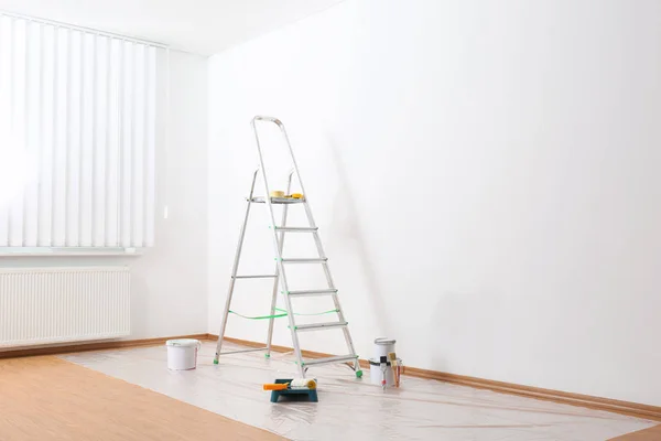 Escadaria e ferramentas de pintura perto da parede na sala vazia — Fotografia de Stock