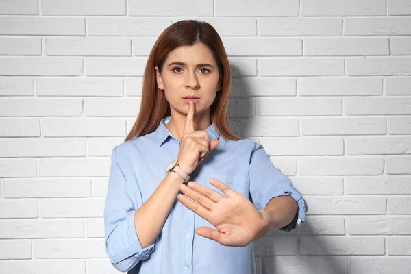 Vrouw toont Hush gebaar in gebarentaal in de buurt van bakstenen muur — Stockfoto