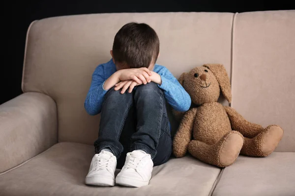 Грустный маленький мальчик с игрушкой сидит дома на диване — стоковое фото