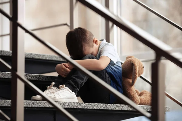 Triste niño con juguete sentado en las escaleras en el interior —  Fotos de Stock