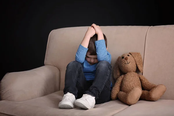 Menino triste com brinquedo sentado no sofá em casa — Fotografia de Stock