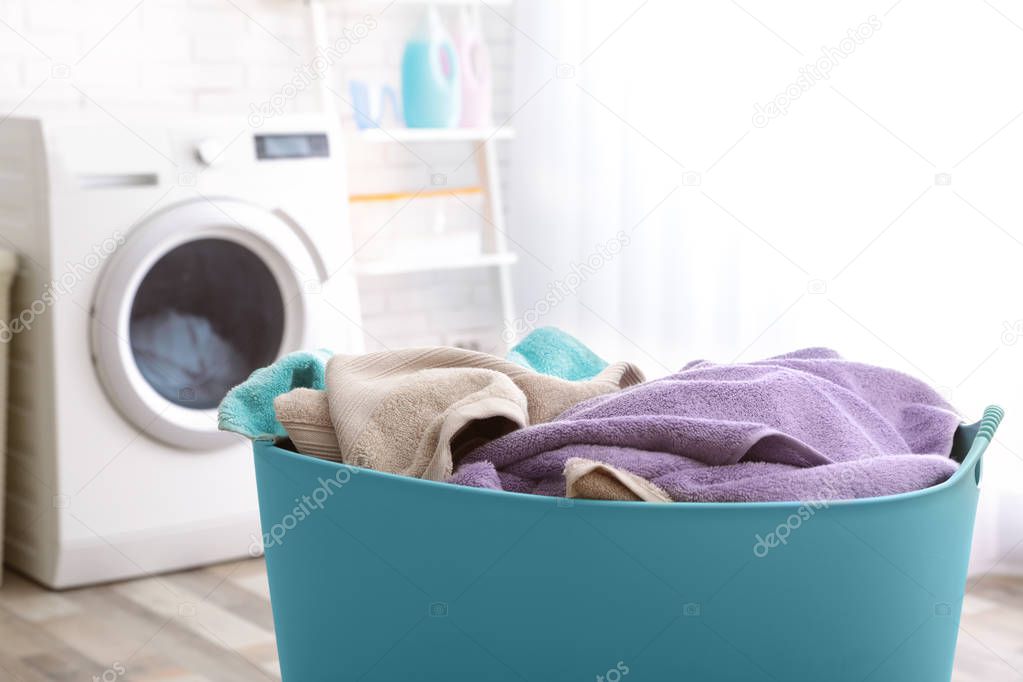 Plastic basket with dirty towels on table in laundry room