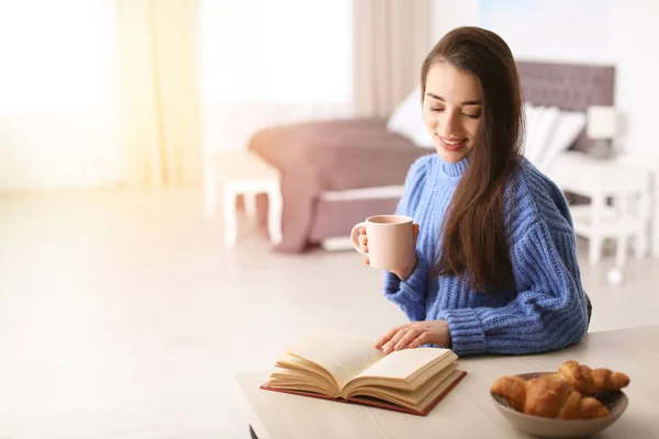 Giovane donna che beve caffè e lettura libro a tavola al chiuso, spazio per il testo — Foto Stock
