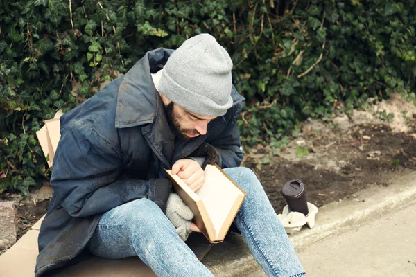 Homem pobre sem-teto com livro na rua na cidade — Fotografia de Stock