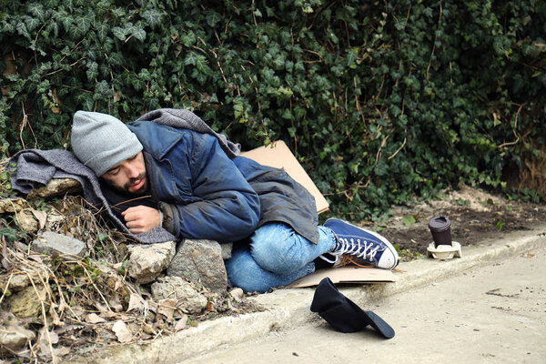 Poor homeless man lying on street in city