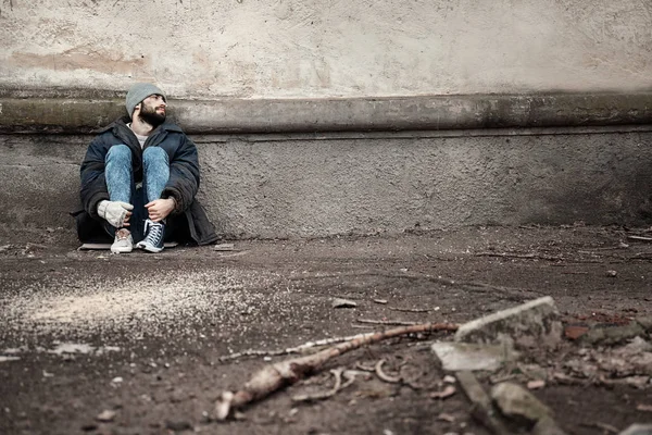 Povero senzatetto seduto vicino al muro sulla strada. Spazio per testo — Foto Stock