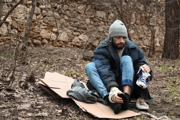 Poor homeless man sitting on cardboard in city park — Stock Photo, Image