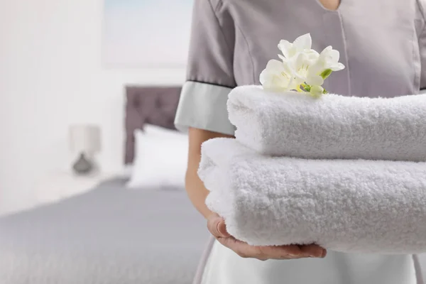 Služebná drží čisté ručníky s květinami v hotelovém pokoji, closeup — Stock fotografie