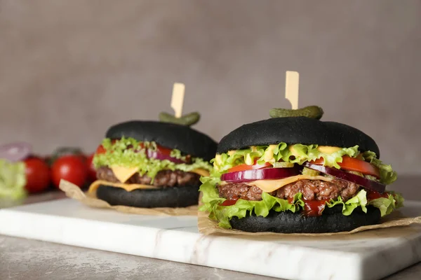 Deska s černými hamburgery na stole proti barevnému pozadí — Stock fotografie