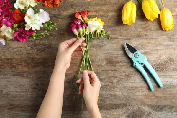 Woman making bouquet of freesia flowers at table, top view — Stock Photo, Image