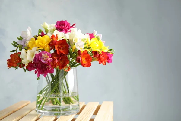 Bouquet of spring freesia flowers in vase on color background. Space for text — Stock Photo, Image