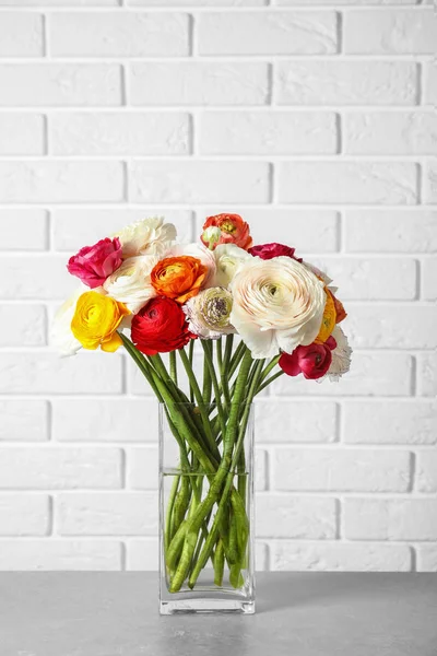 Vase with beautiful spring ranunculus flowers on table near brick wall — Stock Photo, Image