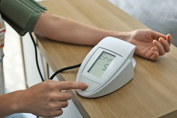 Frau überprüft Blutdruck mit Blutdruckmessgerät am Tisch drinnen, Nahaufnahme. Kardiologie-Konzept — Stockfoto