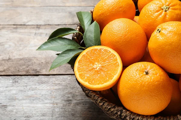 Wicker bowl with ripe oranges on wooden background, closeup. Space for text — Stock Photo, Image