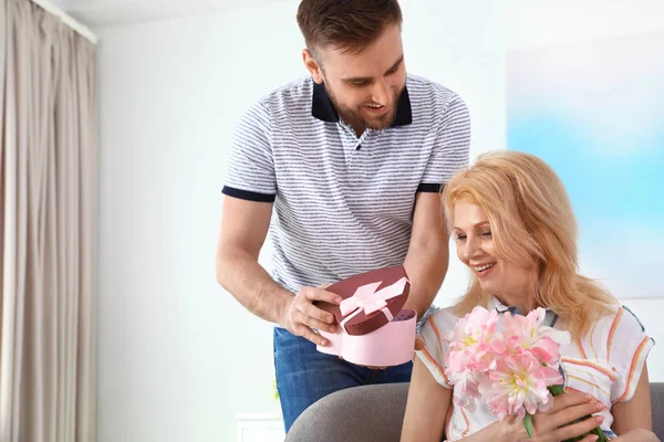 Junger Mann gratuliert seiner erwachsenen Mutter zu Hause, Platz für Text. Glücklicher Muttertag — Stockfoto