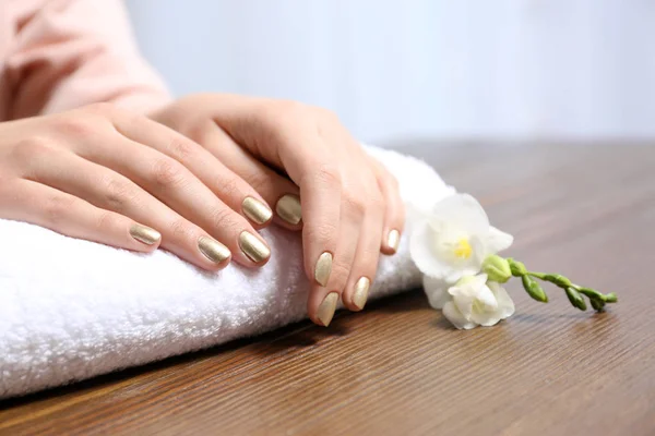 Mujer con manicura dorada en toalla enrollada en la mesa, primer plano. Tendencias de esmalte de uñas — Foto de Stock