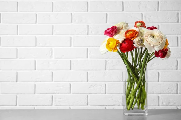 Güzel bahar Ranunculus çiçekleri ile vazo masada tuğla duvar, metin için alan yakın — Stok fotoğraf