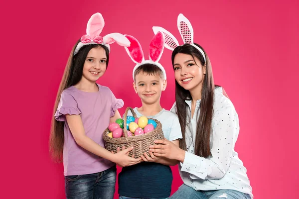 Família bonito em orelhas de coelho headbands com cesta de ovos de Páscoa no fundo de cor — Fotografia de Stock