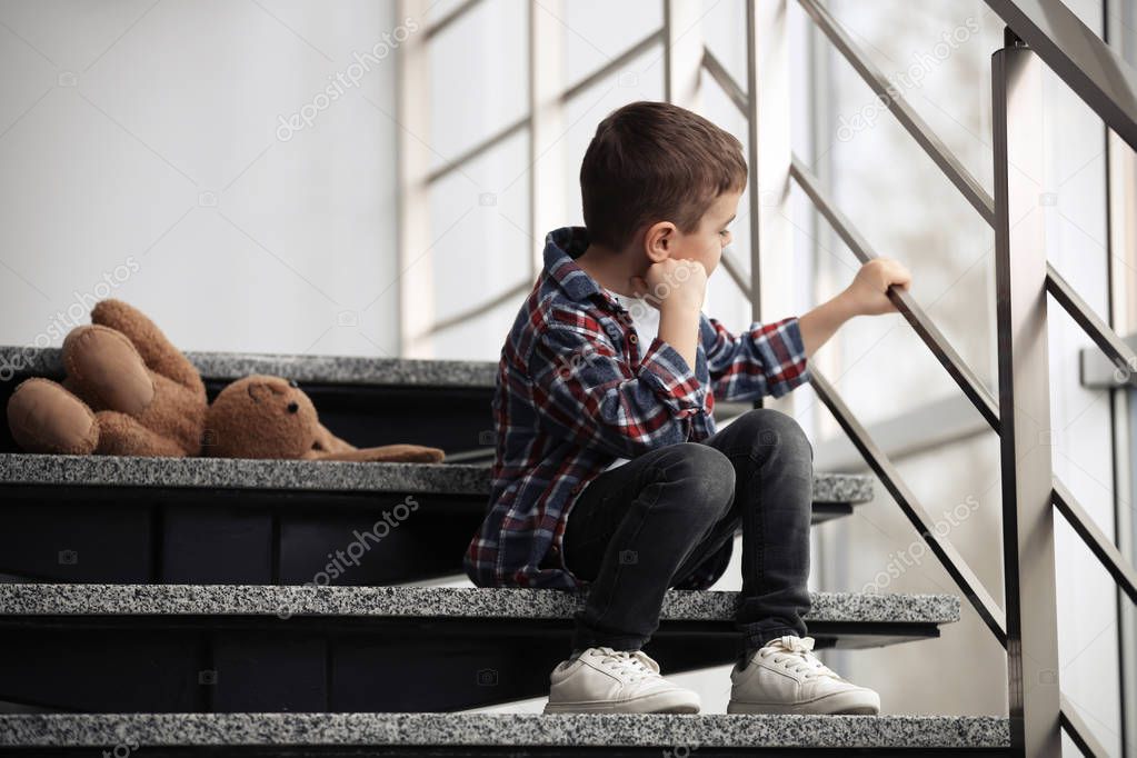 Sad little boy with toy sitting on stairs indoors