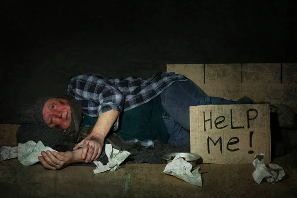Бедняга, лежащий рядом с картонной табличкой, помогите мне на полу. — стоковое фото