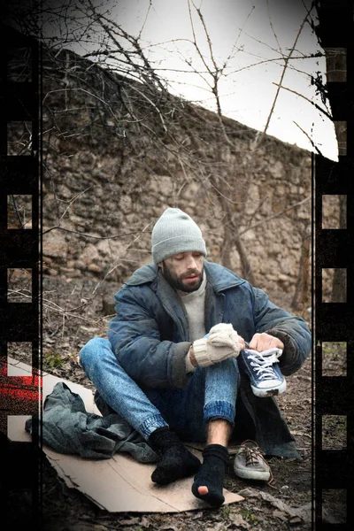 Бедный бездомный сидит на картонке в городском парке — стоковое фото