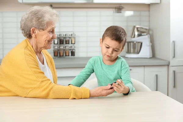 Femme âgée avec son petit-fils utilisant un glucomètre numérique à la maison. Contrôle du diabète — Photo