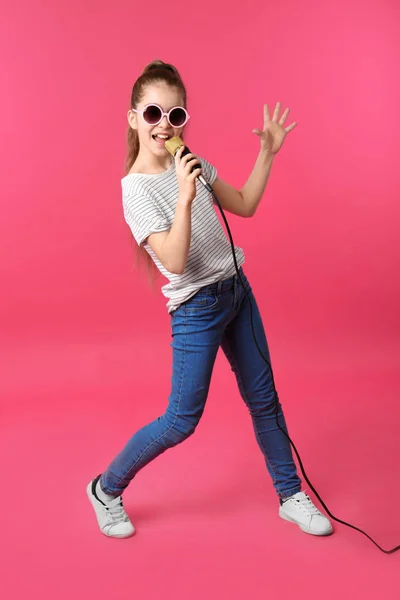 Menina bonito cantando em microfone no fundo de cor — Fotografia de Stock