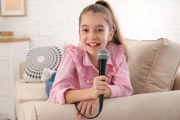 Nettes Mädchen mit Mikrofon auf Sofa im Wohnzimmer — Stockfoto