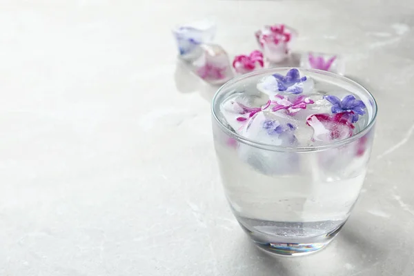 Glas vatten med blommiga isbitar på bordet. Utrymme för text — Stockfoto