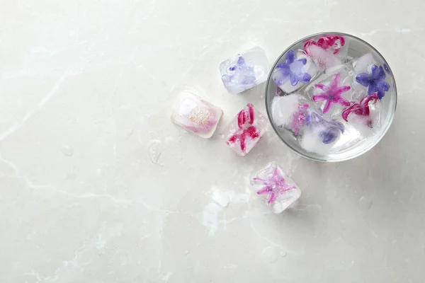 Vaso de agua y cubitos de hielo con flores en la mesa, vista superior. Espacio para texto — Foto de Stock