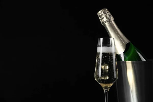 Glas Champagne in de buurt emmer met fles op zwarte achtergrond, ruimte voor tekst — Stockfoto