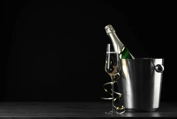 Verre de champagne près seau avec bouteille sur fond noir, espace pour le texte — Photo