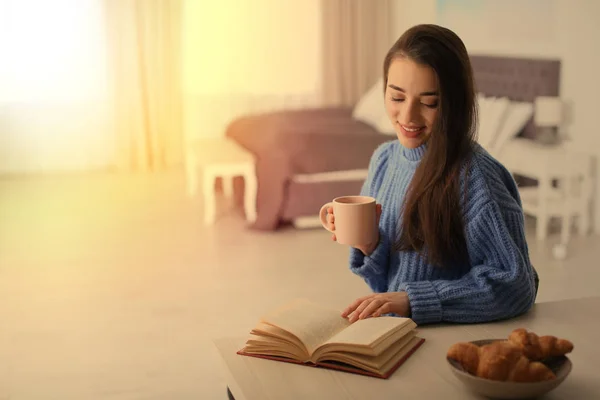 Giovane donna che beve caffè e lettura libro a tavola al chiuso, spazio per il testo — Foto Stock