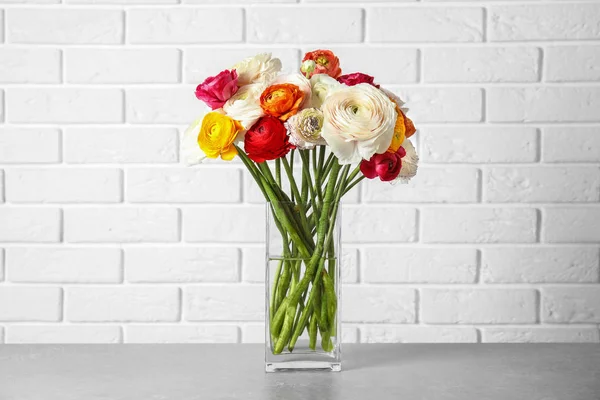 Jarrón con hermosas flores ranúnculo primavera en la mesa cerca de la pared de ladrillo — Foto de Stock