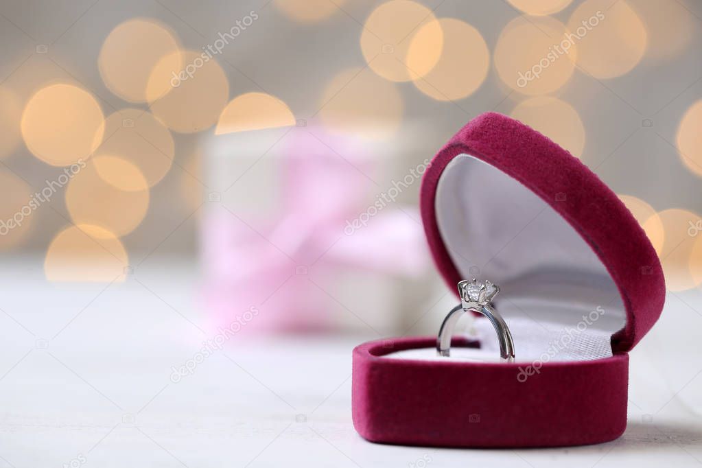 Box with ring on table against blurred lights. Space for text