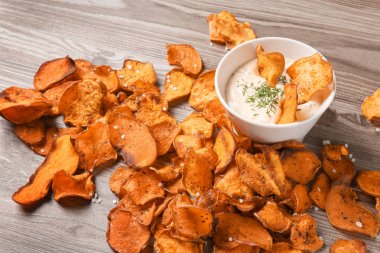 Ahşap arka planda tatlı patates cips ve sos kase