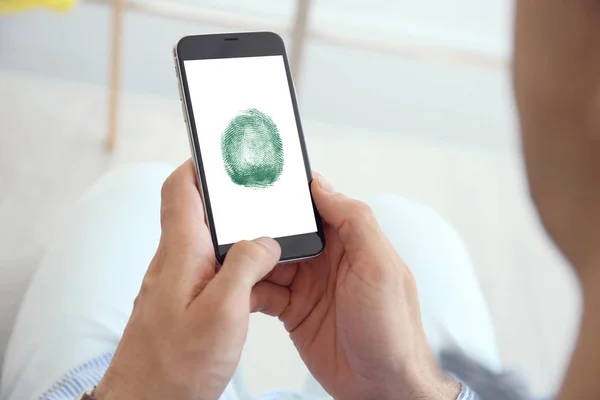 Man holding mobile phone with fingerprint sensor indoors, closeup