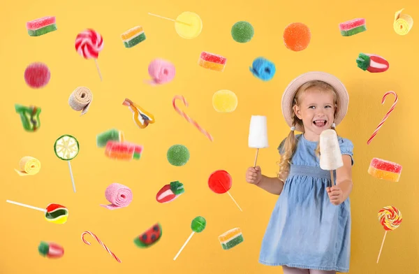 Adorable petite fille avec barbe à papa et bonbons volants sur fond de couleur — Photo