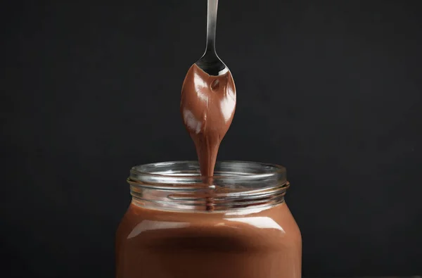 Menuang krim coklat manis ke dalam botol kaca dengan latar belakang gelap — Stok Foto
