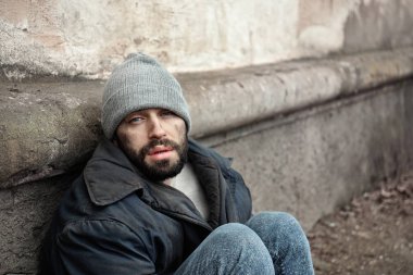 Sokakta duvarın yanında oturan zavallı evsiz adam. Metin alanı