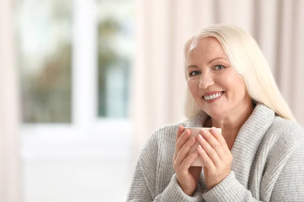 Retrato de una hermosa mujer mayor con una taza de té sobre un fondo borroso. Espacio para texto — Foto de Stock